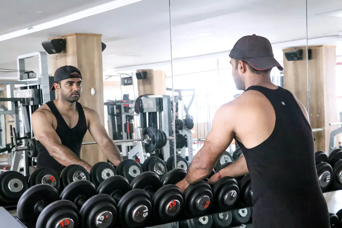 A man choosing dumbbells from a rack in a gym, reflected in the mirror