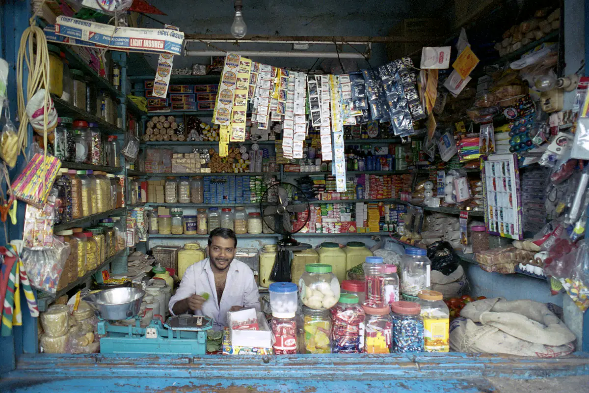 A shopkeeper smiling behind the counter of a small, fully stocked general store